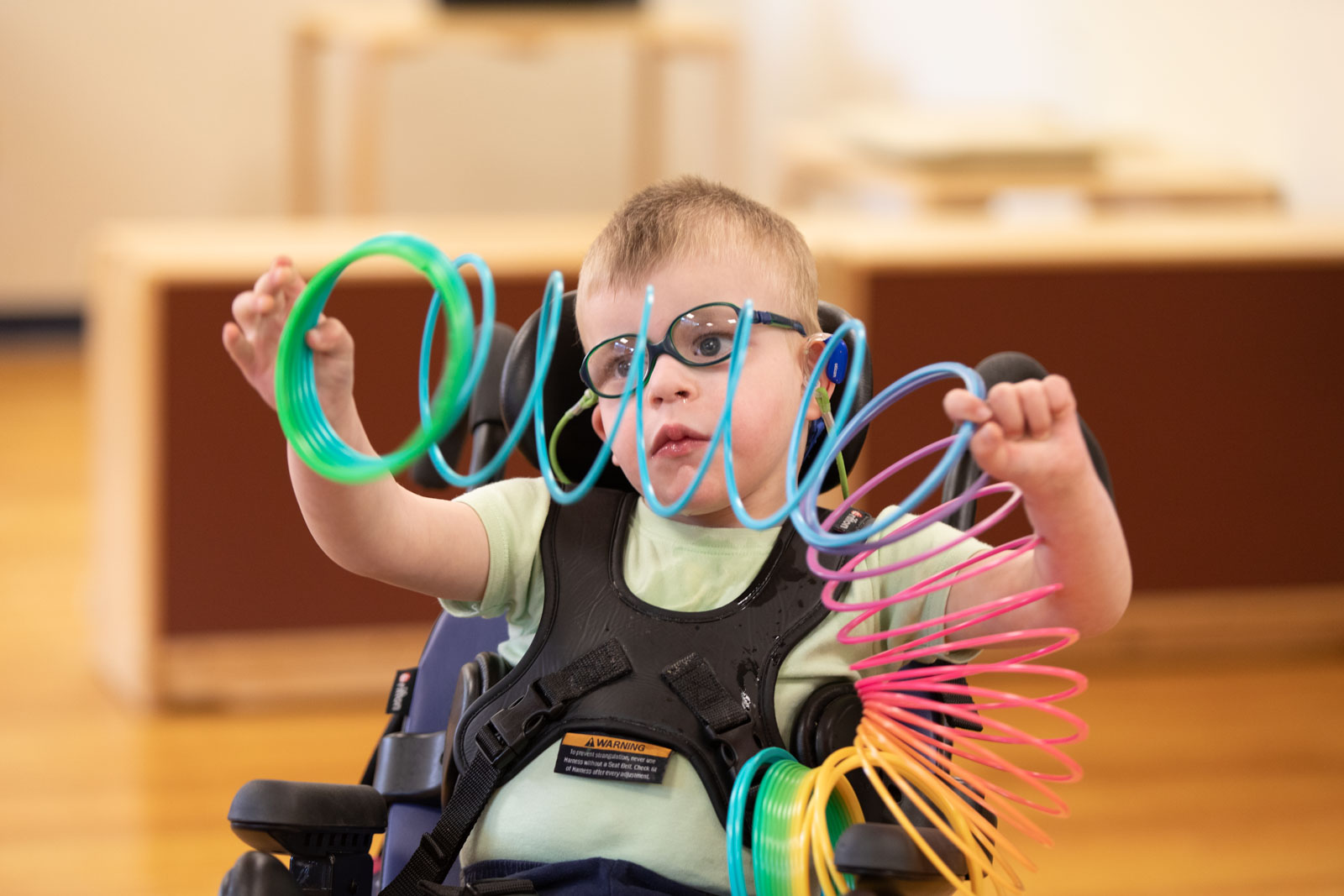A young boy with glasses holds up a colorful slinky.